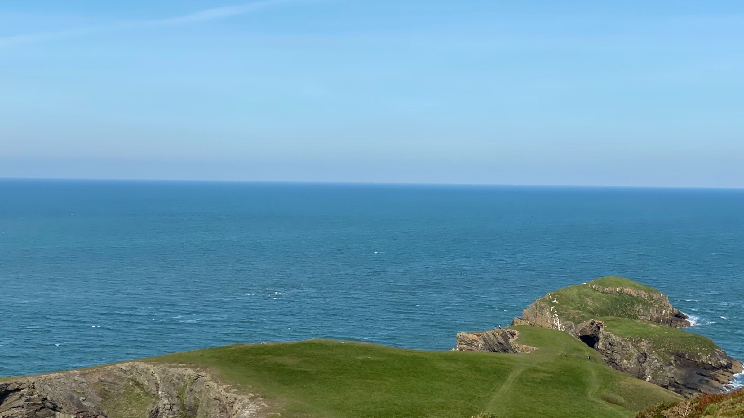 A green headland above the calm, open water of Cardigan Bay under a clear blue sky